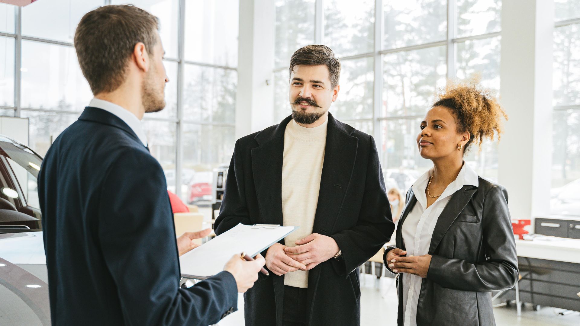 Happy couple discussing car purchase with dealer in showroom. Professional interaction and consultation.