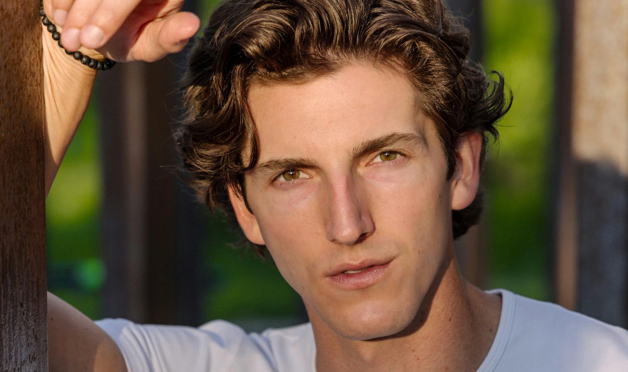 A young man in a white shirt leaning against a fence