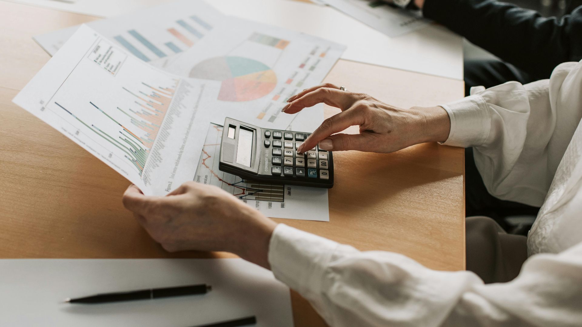 Hands performing financial calculations with charts and a calculator at a meeting table.