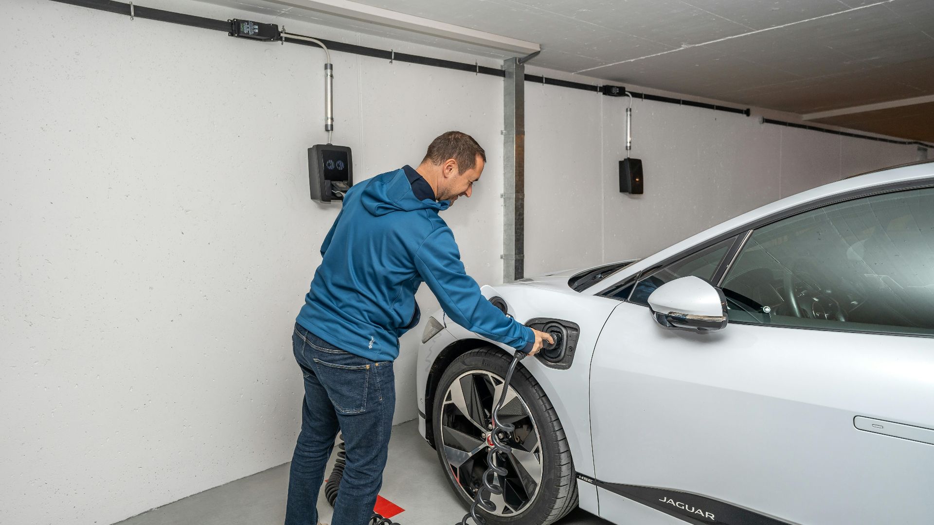 A man connects an electric car to a charging station in a modern indoor garage setting.
