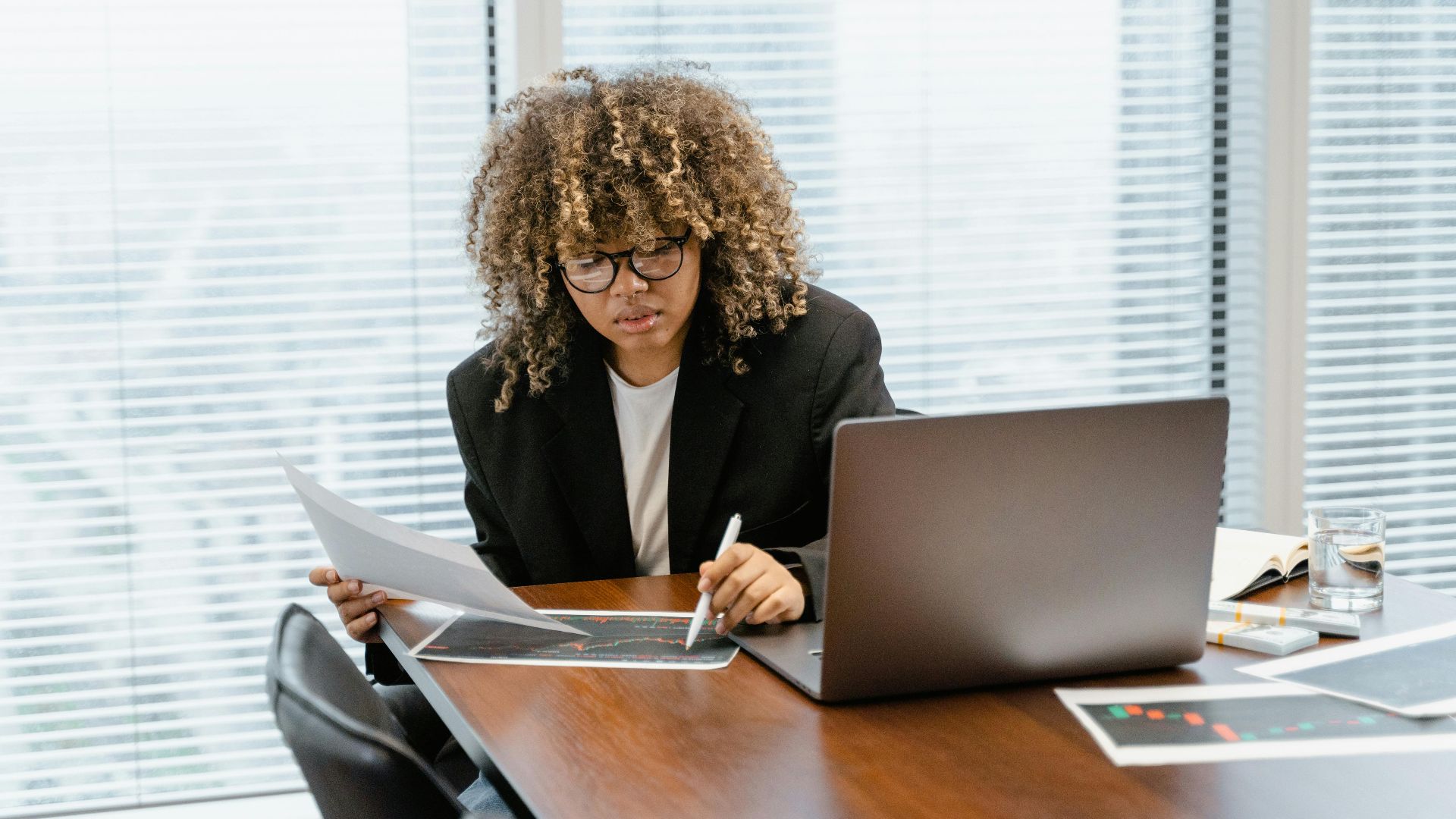 A young professional analyzing financial charts at a modern office desk with a laptop.