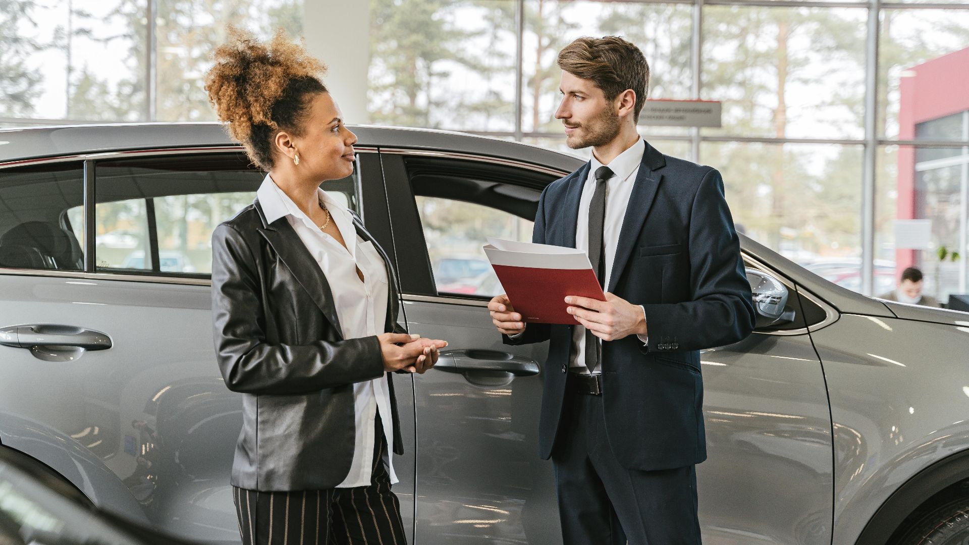 A woman discussing car purchase with a dealer inside a car dealership showroom.