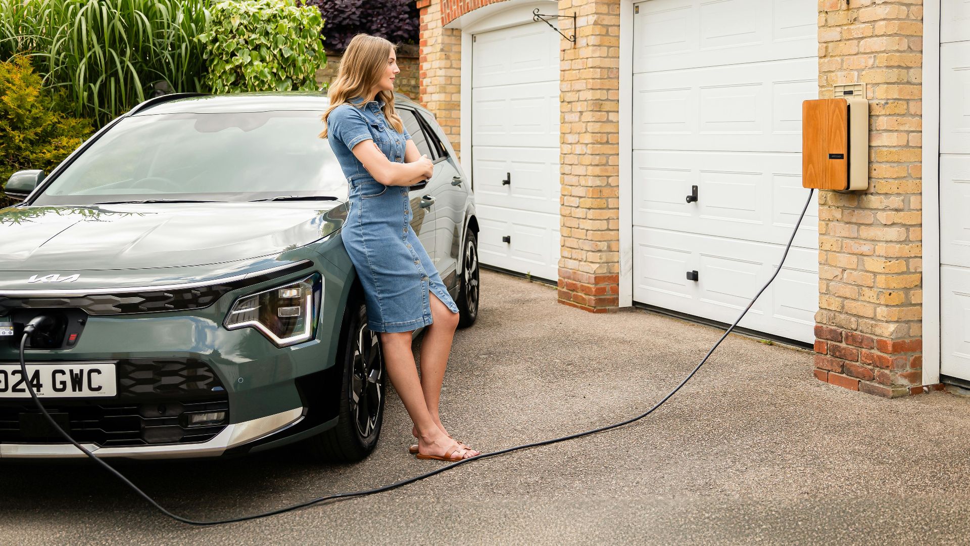 Woman charging electric vehicle at home with a modern wall-mounted charging station.