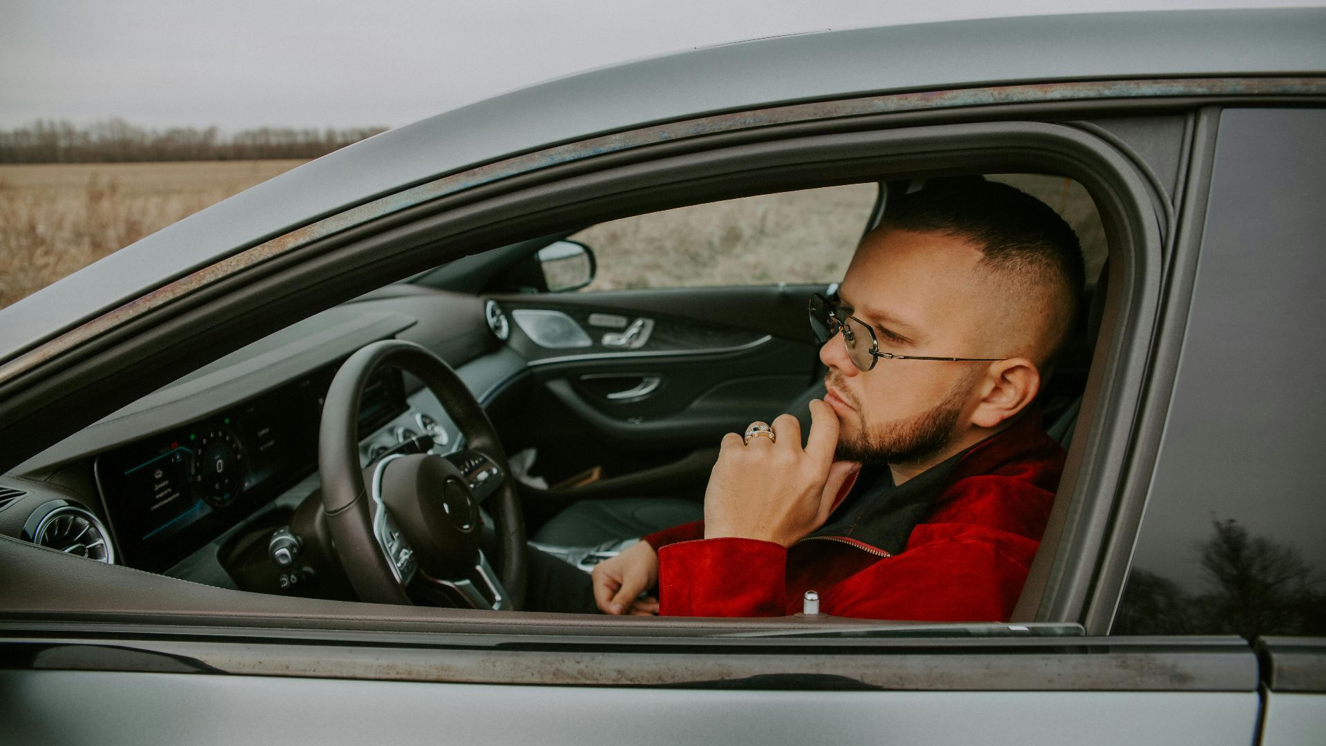 Side view of thoughtful young bearded male in eyeglasses sitting in driver seat of car