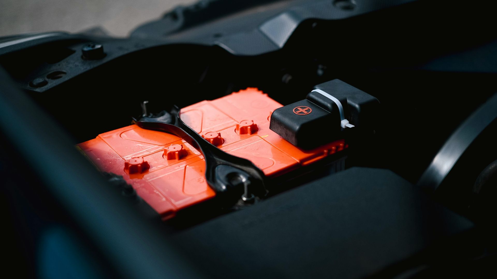 Detailed view of an orange car battery inside a vehicle's engine bay, highlighting its features.