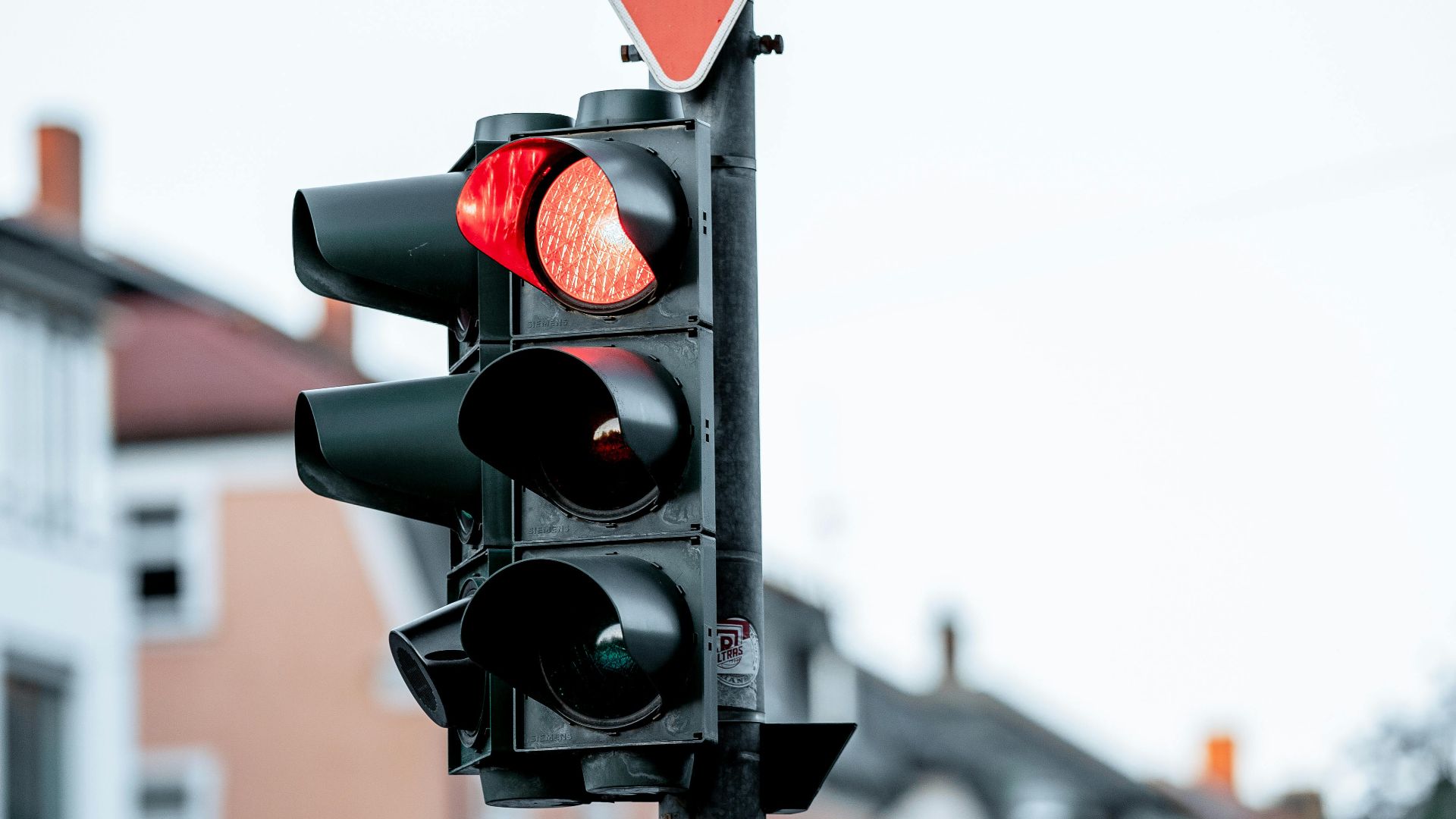 Traffic light with red signal and yield sign against blurred urban background. Ideal for transportation themes.
