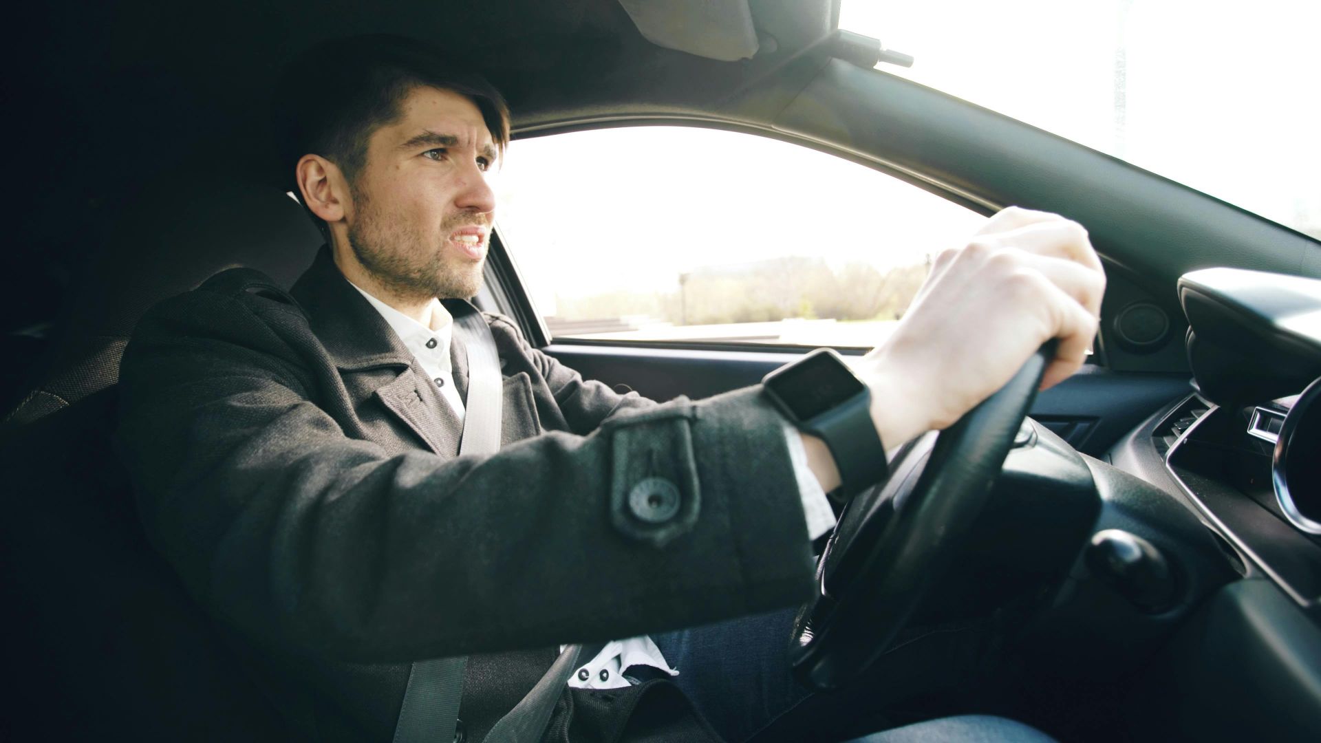 A man driving a car, wearing a wristwatch, focused on the road.