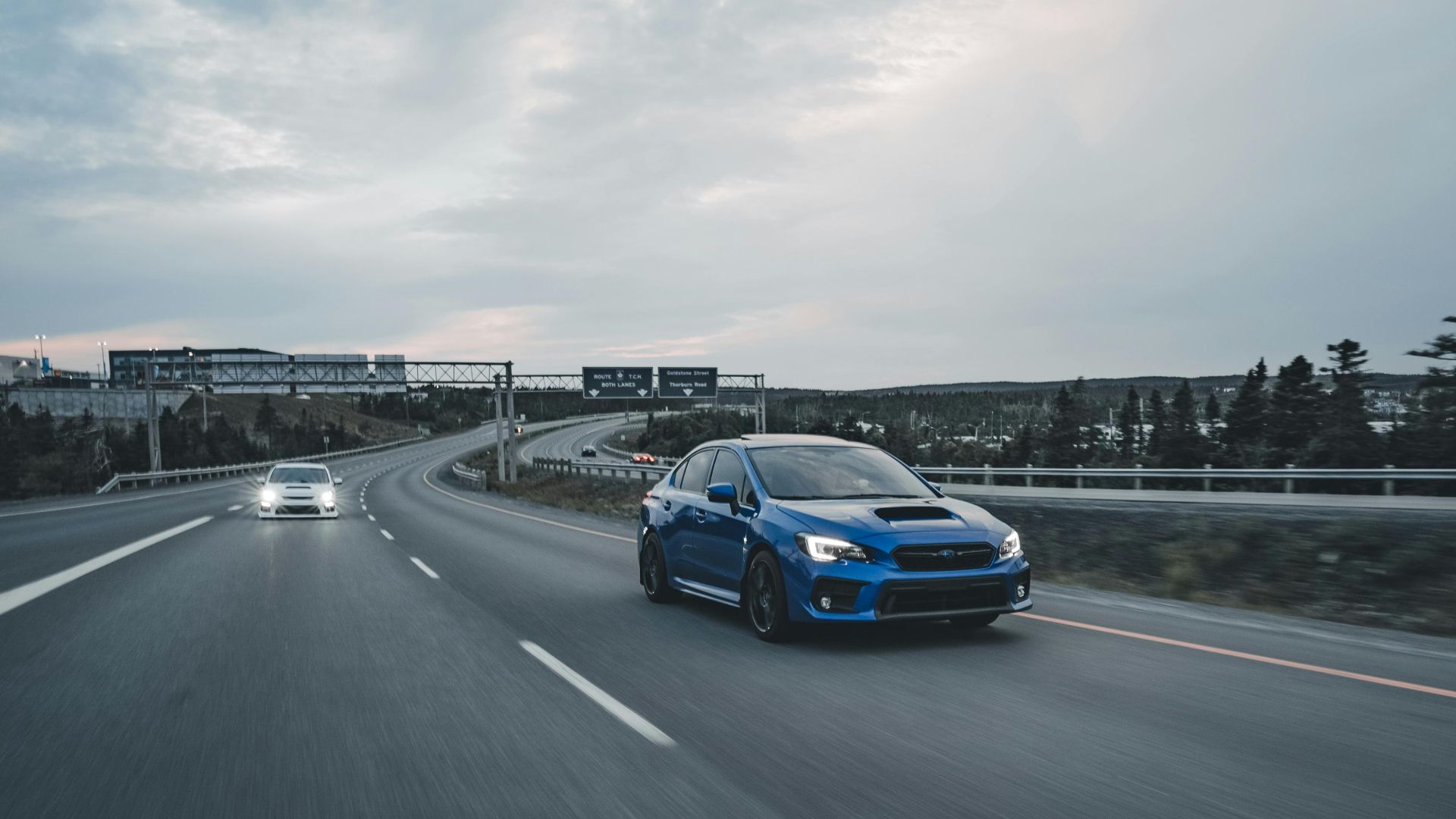 A blue Subaru WRX drives on an empty highway during dusk, showcasing speed and performance.