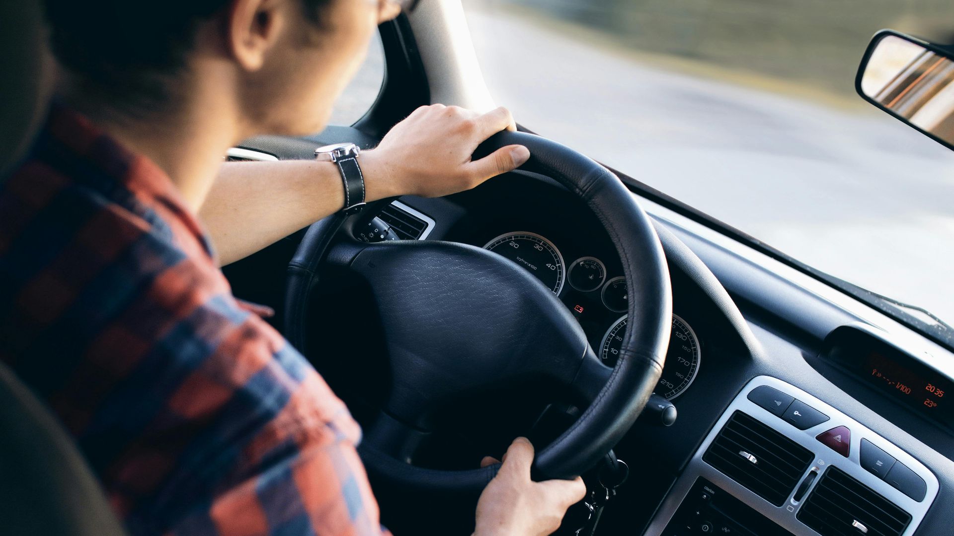 Close-up view of a man driving a modern car, showing dashboard and steering details.