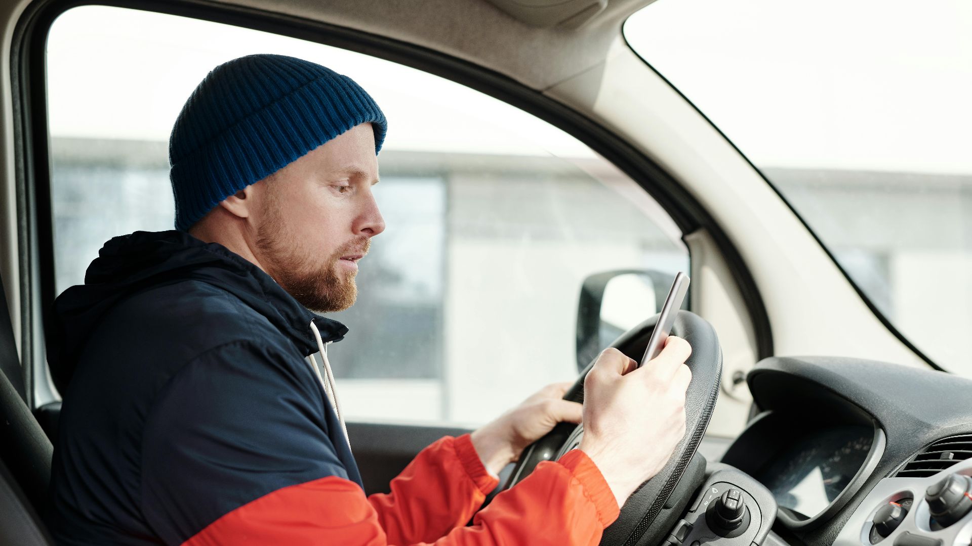 Distracted driver uses a smartphone in a car, highlighting road safety concerns.