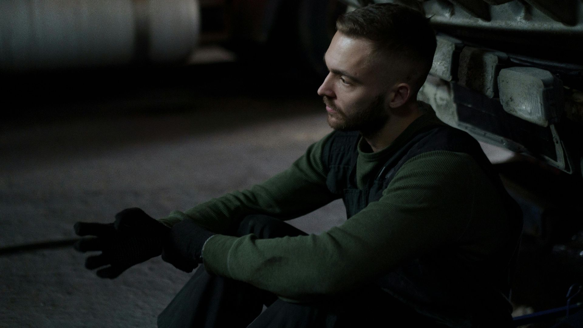 A focused auto mechanic in deep thought during a work break in a dimly lit workshop.