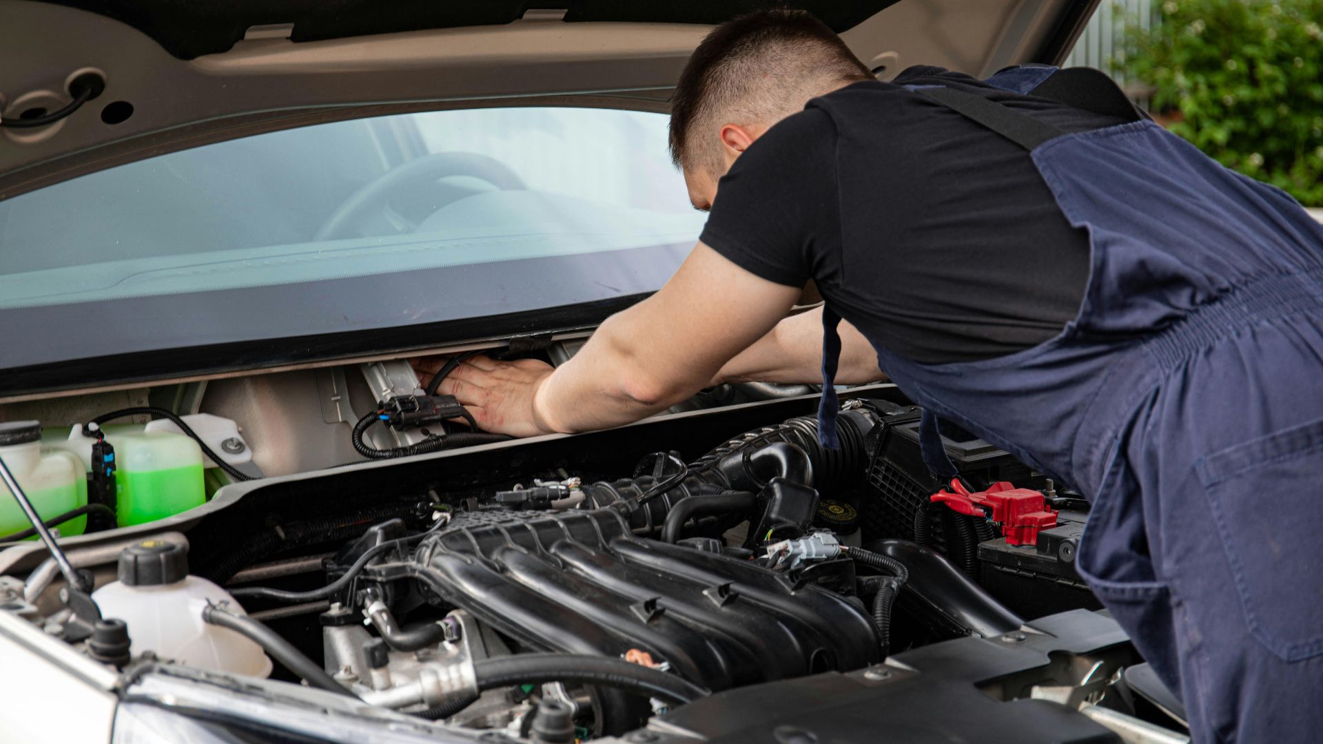 Auto mechanic performs engine maintenance on a car. Focus on hands and engine components.