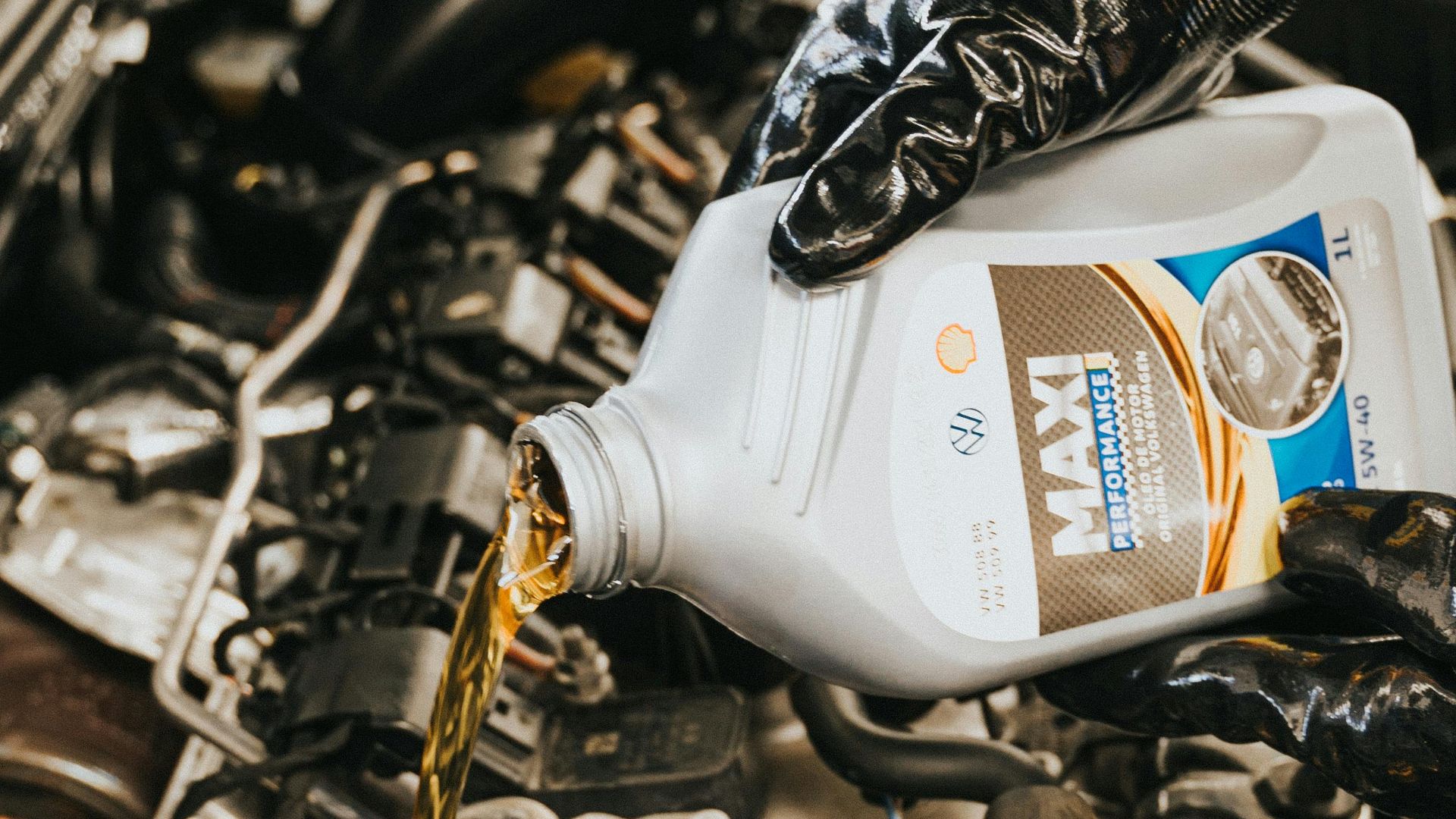 Close-up of mechanic pouring engine oil into car engine with gloved hands, showcasing automotive maintenance.