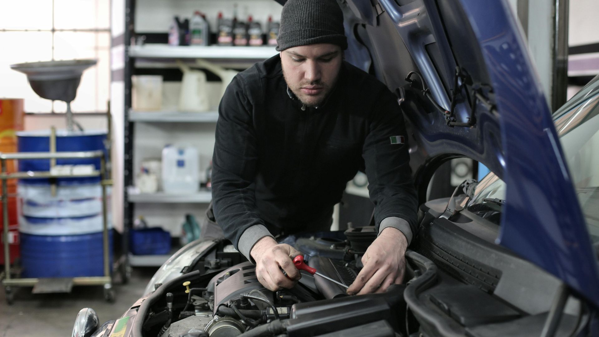 Man working under car hood in a garage, focused on engine repair