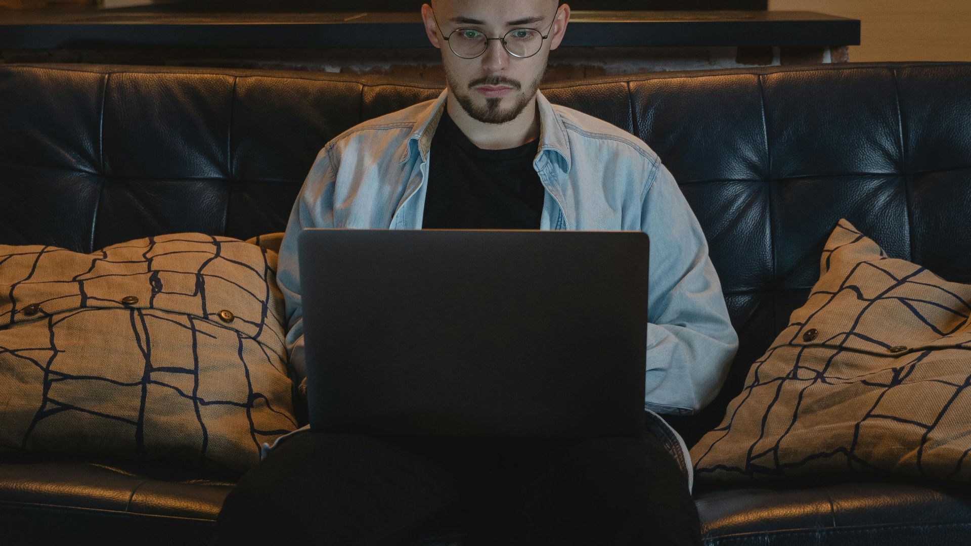 Man working remotely on a laptop in a cozy, stylish apartment with exposed brick walls and modern decor.