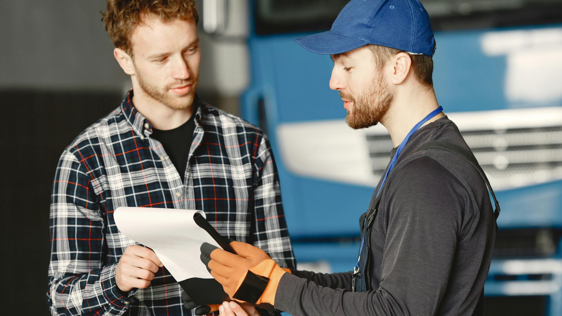 Mechanic in uniform talks with a customer about vehicle maintenance inside a garage.