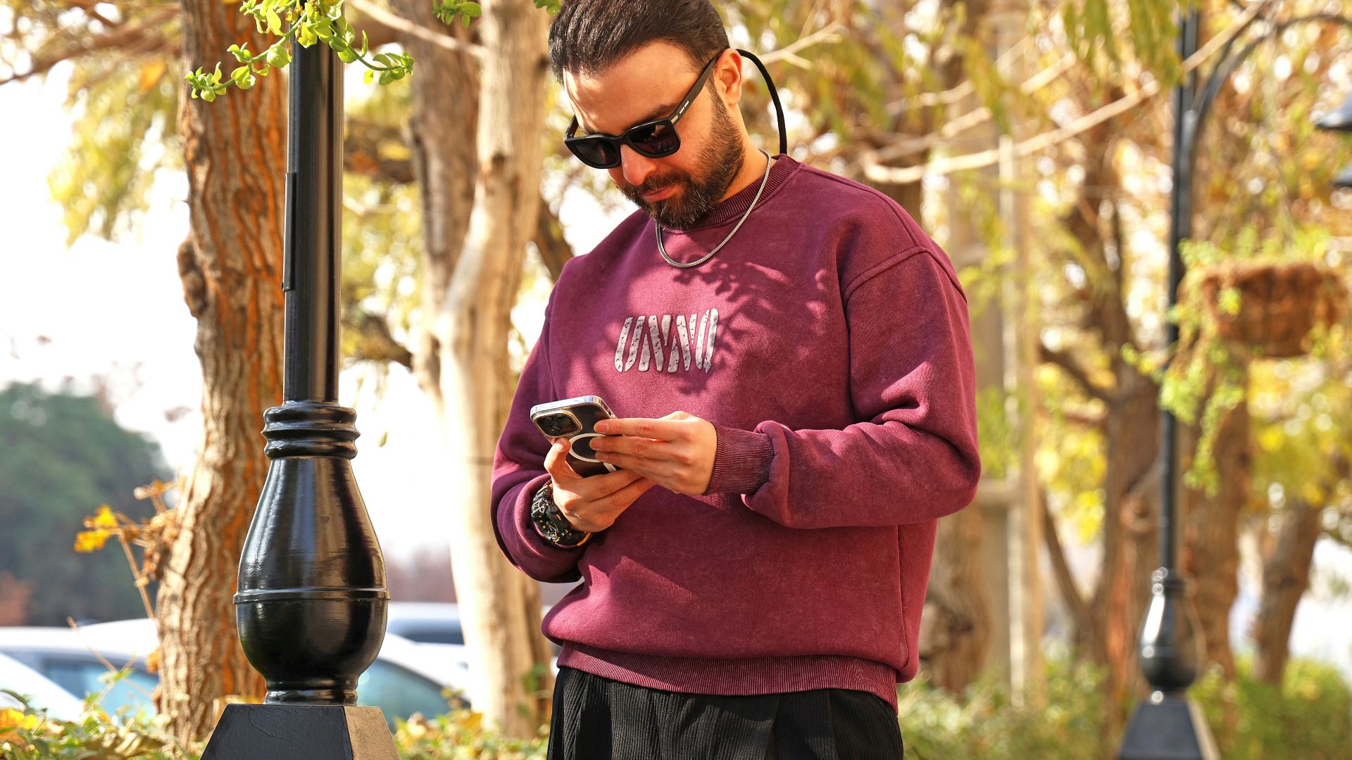 Man in sunglasses looking at his phone outdoors.