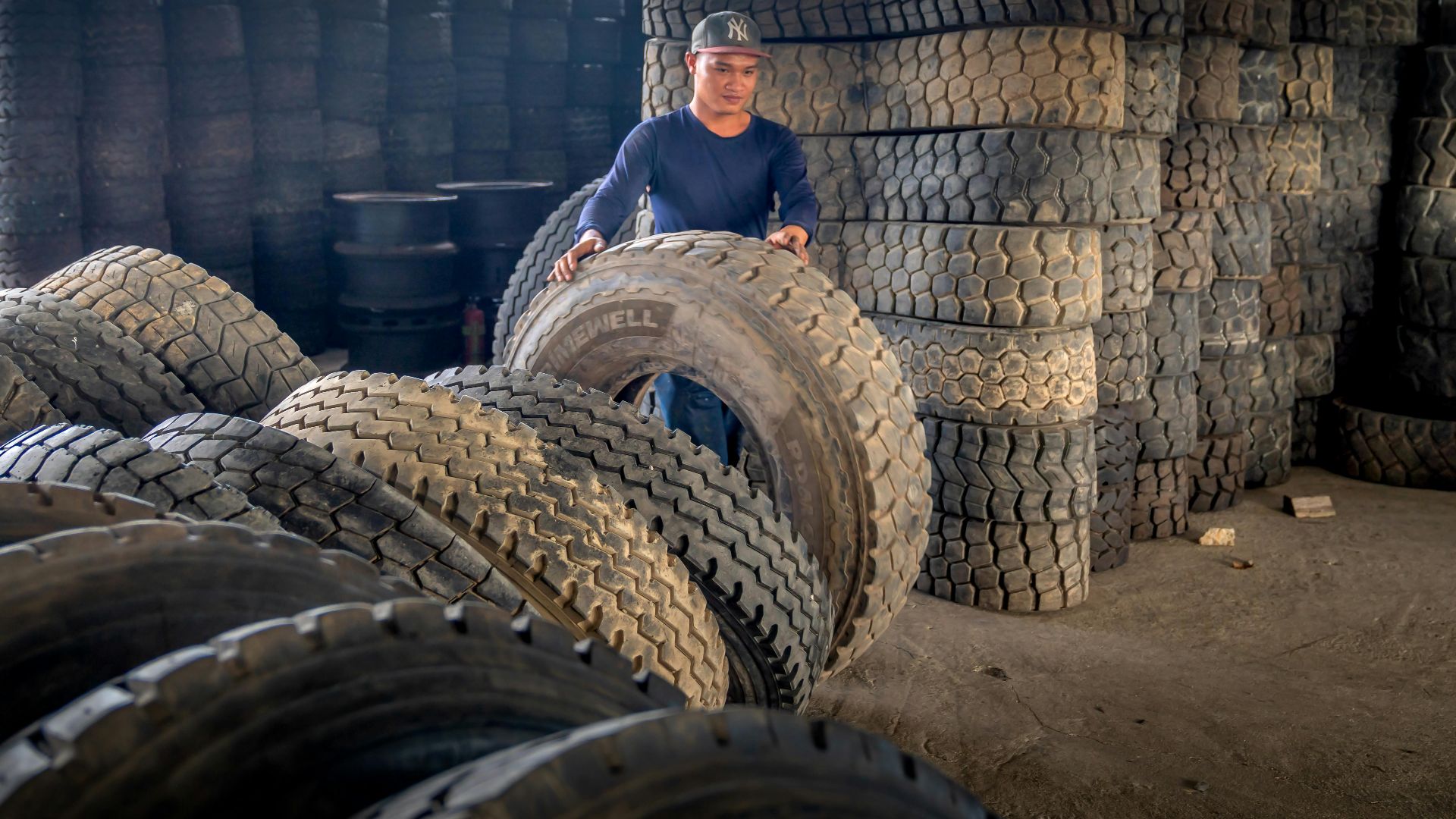 Man organizing large industrial tires in a warehouse, showcasing labor and storage setup.