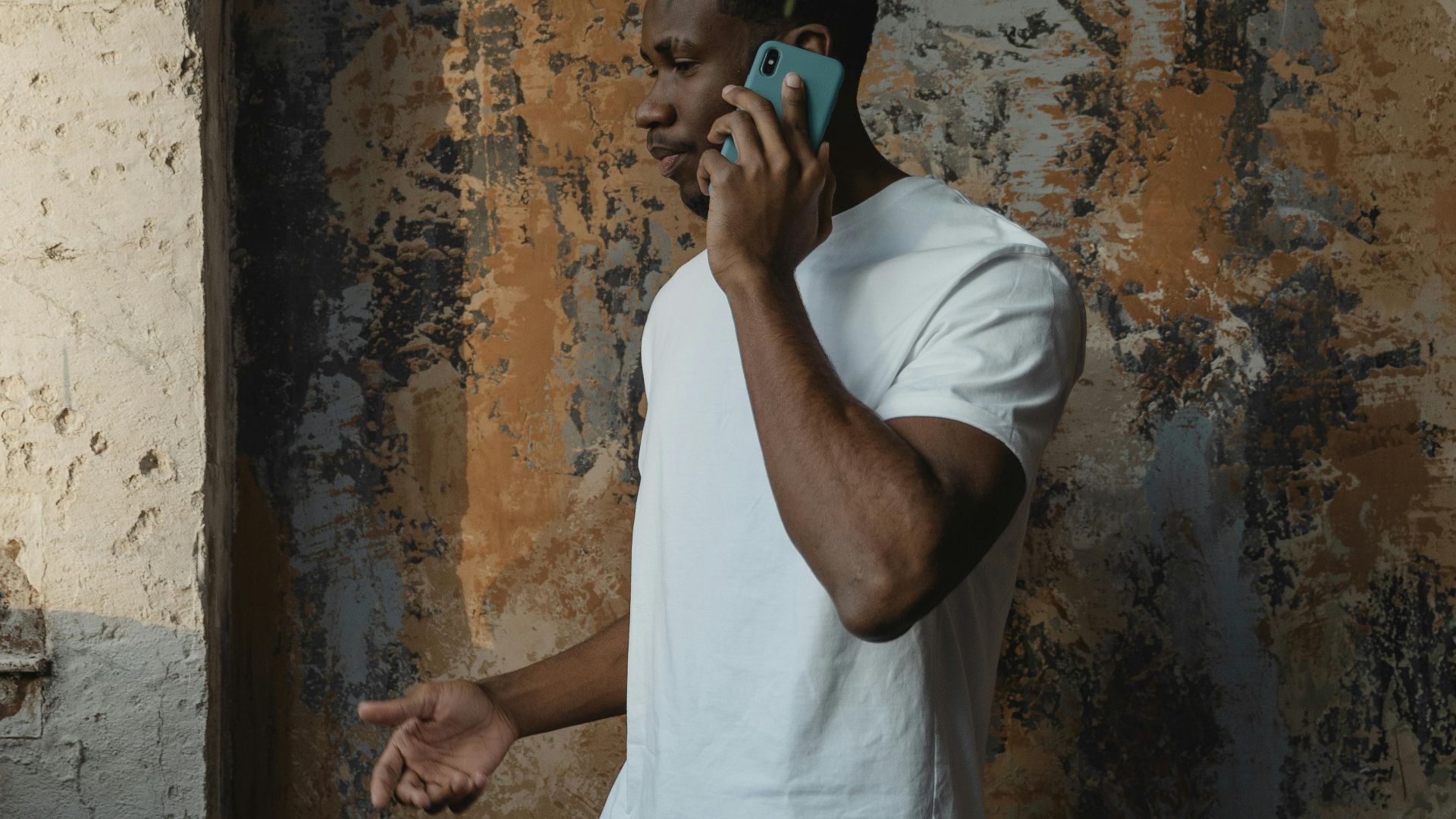African American man in white shirt talking on a cellphone in an indoor setting.