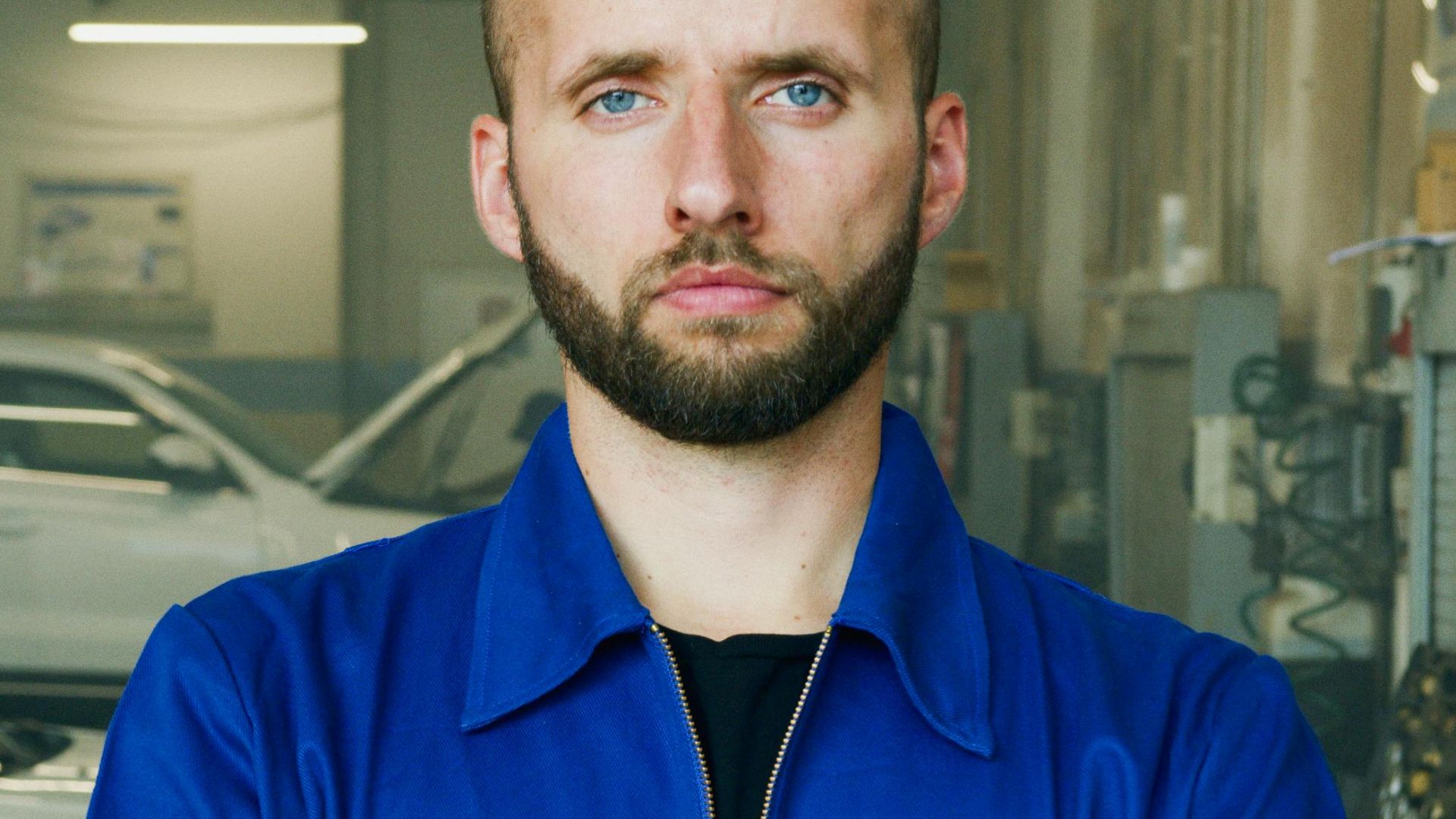 Professional mechanic in blue uniform standing in a garage with arms crossed. Focused and skilled representation.