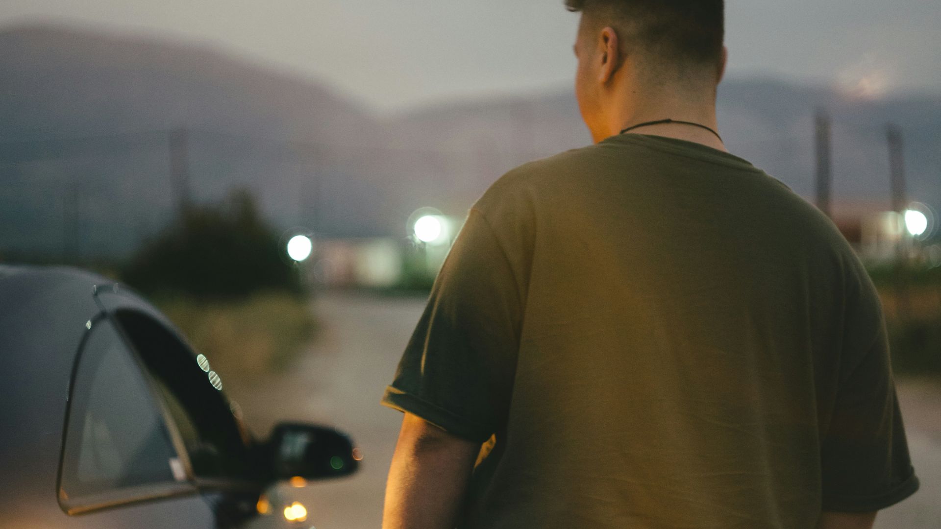 man in green t-shirt standing near black car during daytime