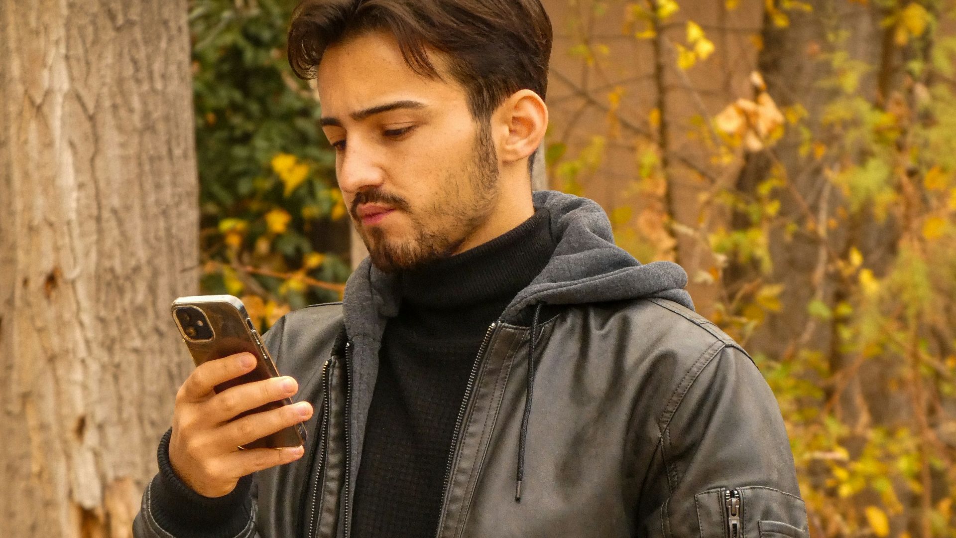 A man standing in a forest looking at his cell phone