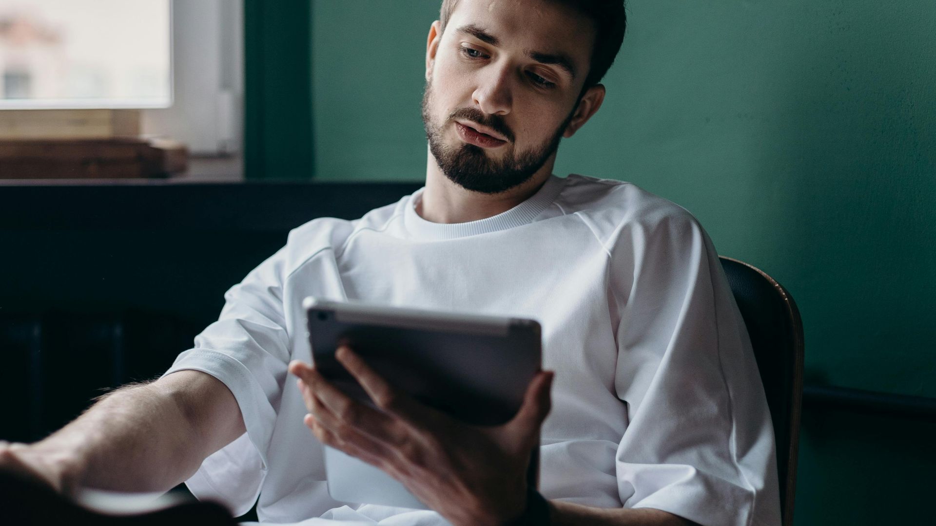 Pensive man using a tablet while relaxing at home. Modern lifestyle concept.