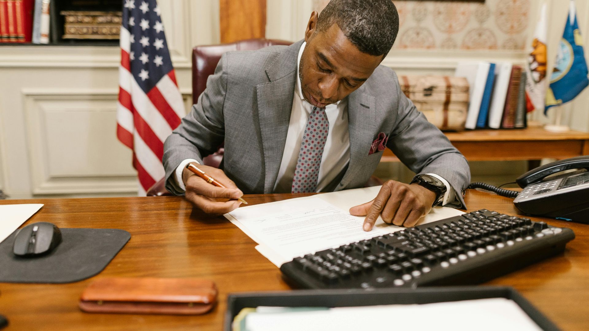 Professional man signs contract at desk in classic office environment.