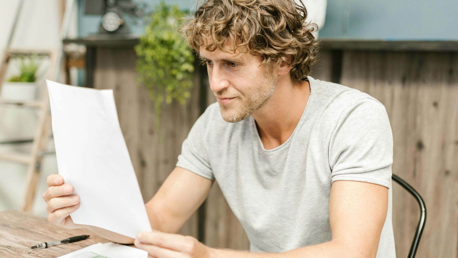 A man with curly hair evaluates documents at a desk, highlighting focused work in a professional setting.