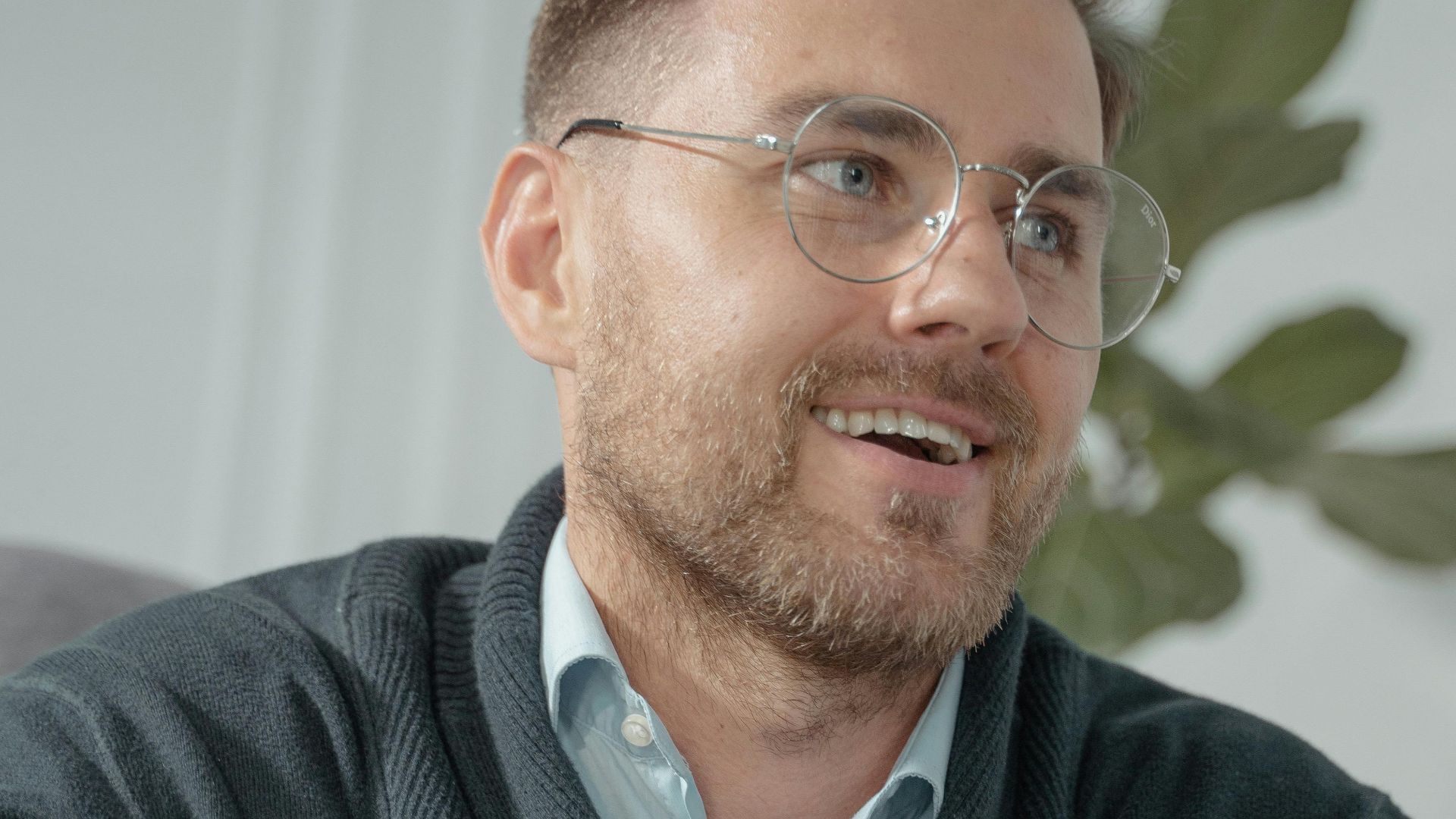 Portrait of a cheerful man with glasses and sweater, indoors.