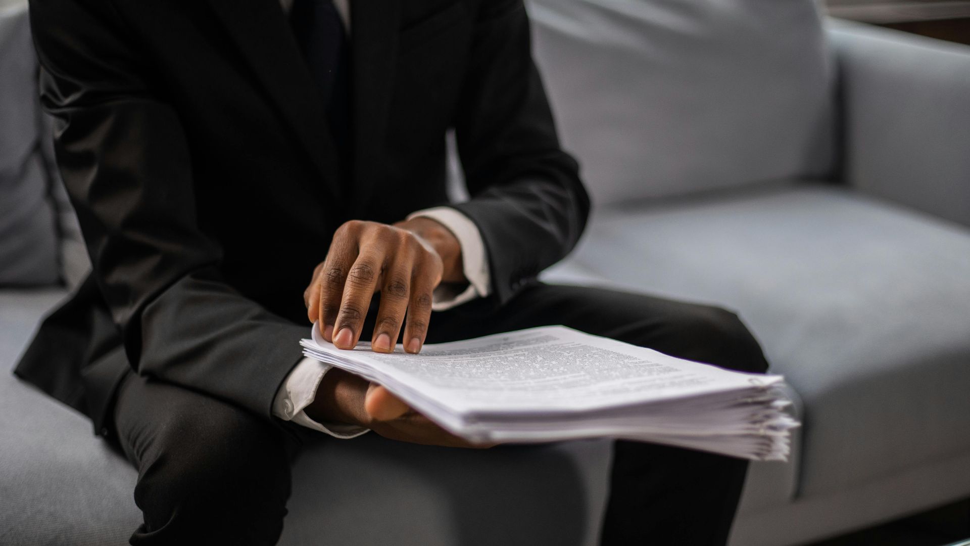 Close-up of a businessman in a suit reviewing documents while seated on a sofa indoors.