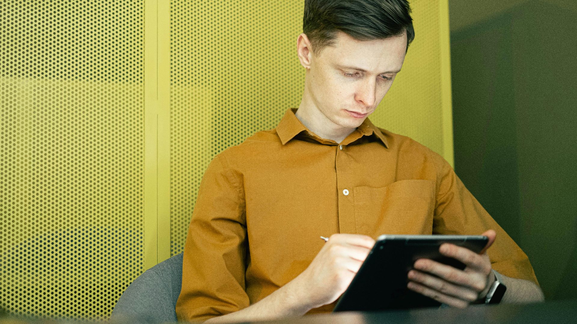 Young man in yellow shirt focused on using a tablet indoors, showcasing modern technology and study.