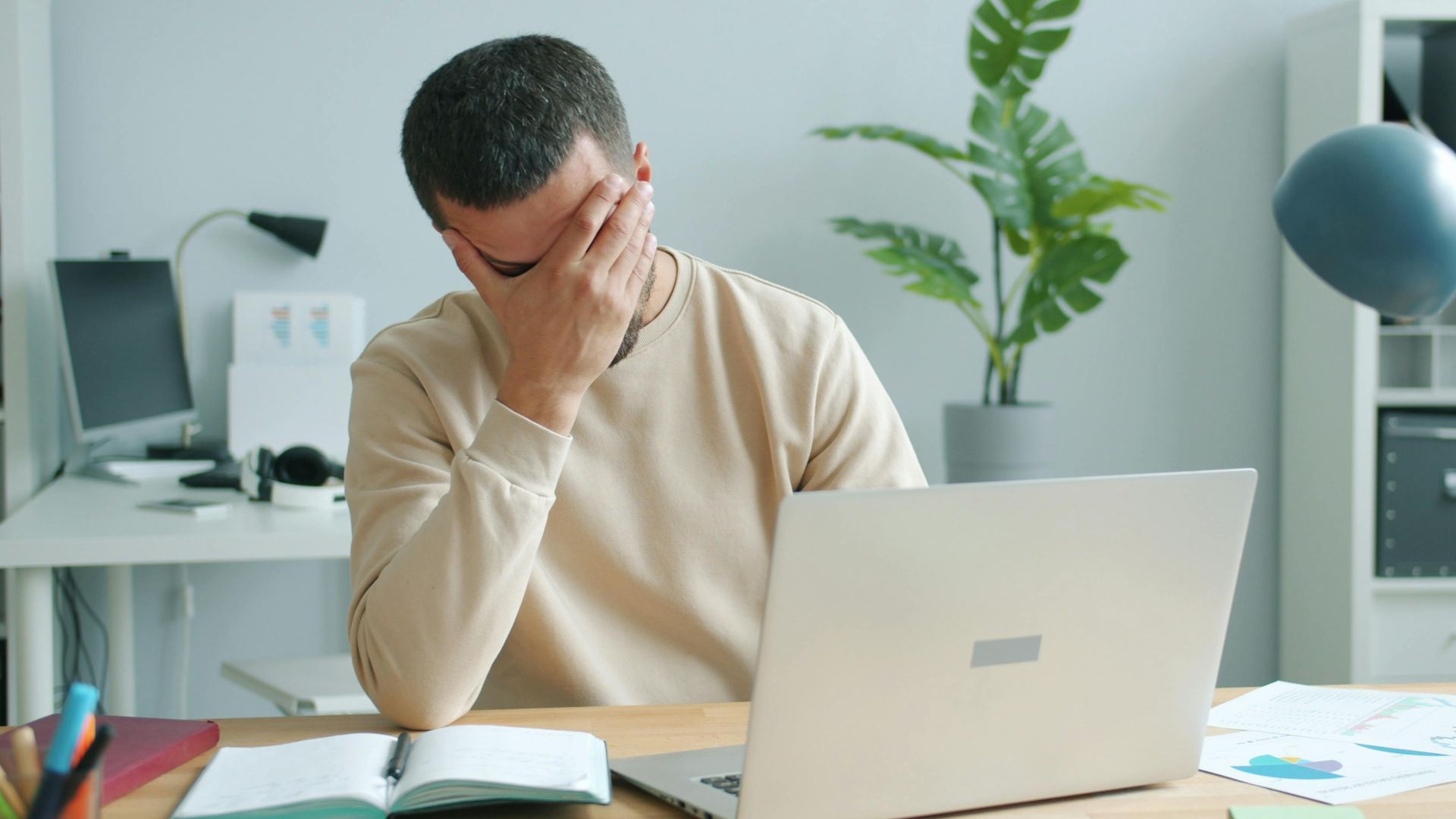 Young man overwhelmed at his desk with laptop, office stress.