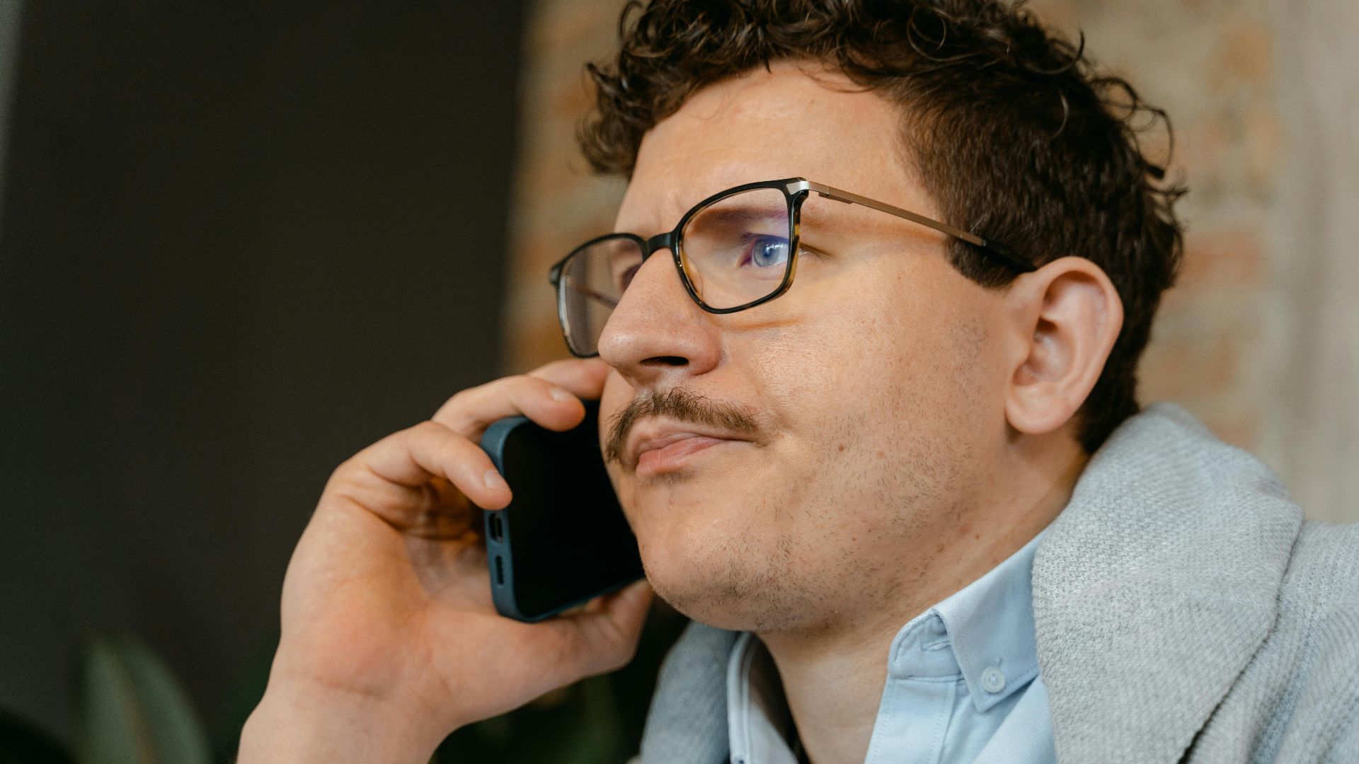 Man with glasses and mustache making a smartphone call indoors.