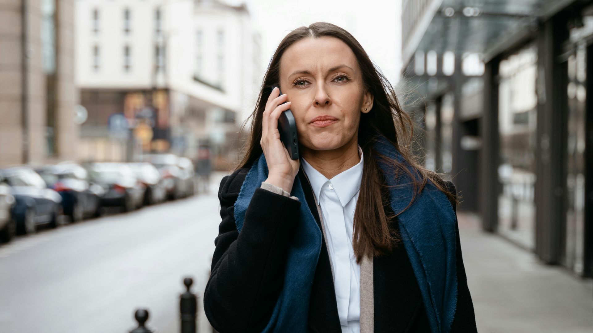 Professional woman walking in urban setting, engaged in cellphone conversation.