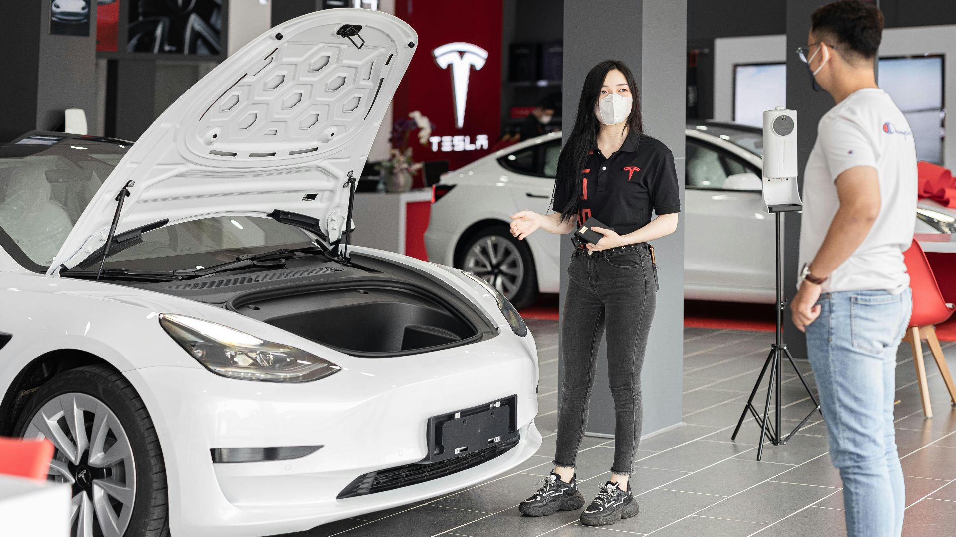 A customer talks with a sales representative about a Tesla Model 3 in a car dealership, showcasing the electric car's features.