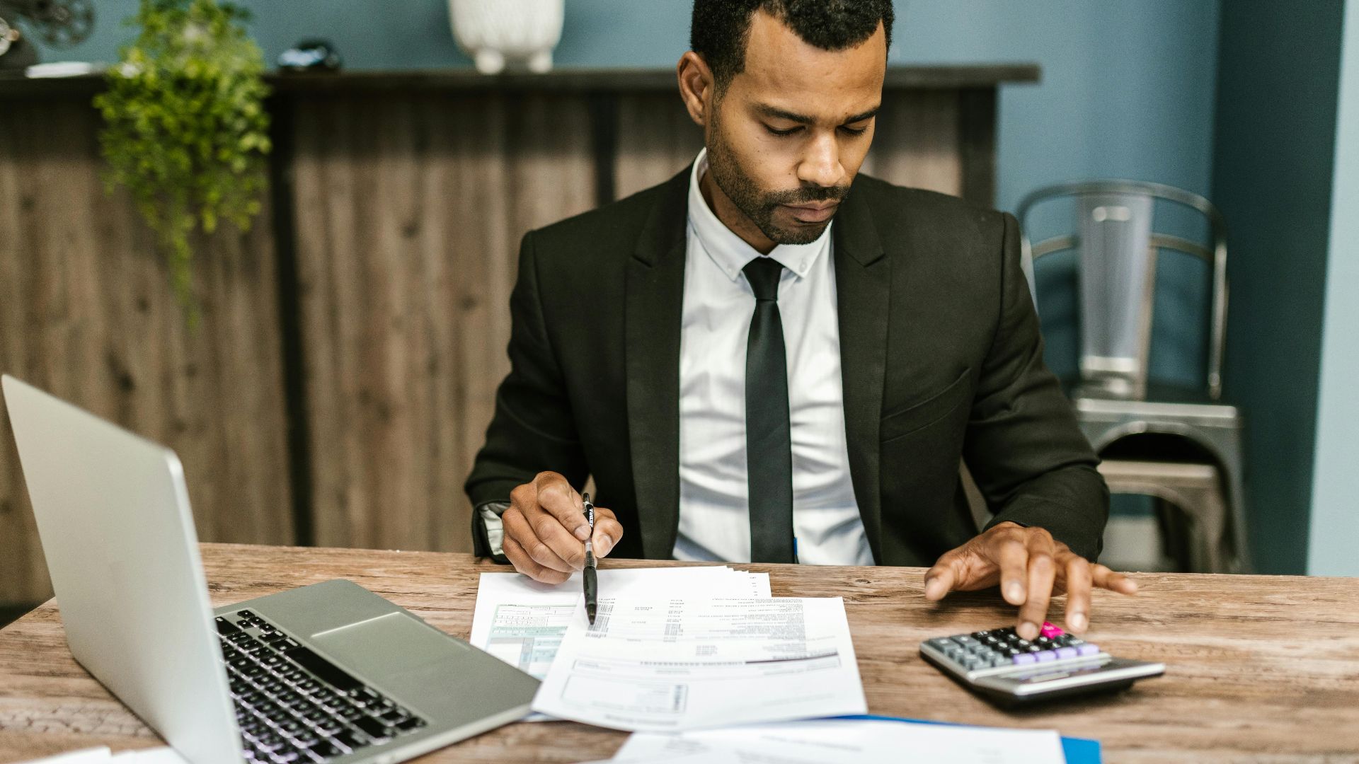 A focused businessman works with a calculator and documents in a modern office.