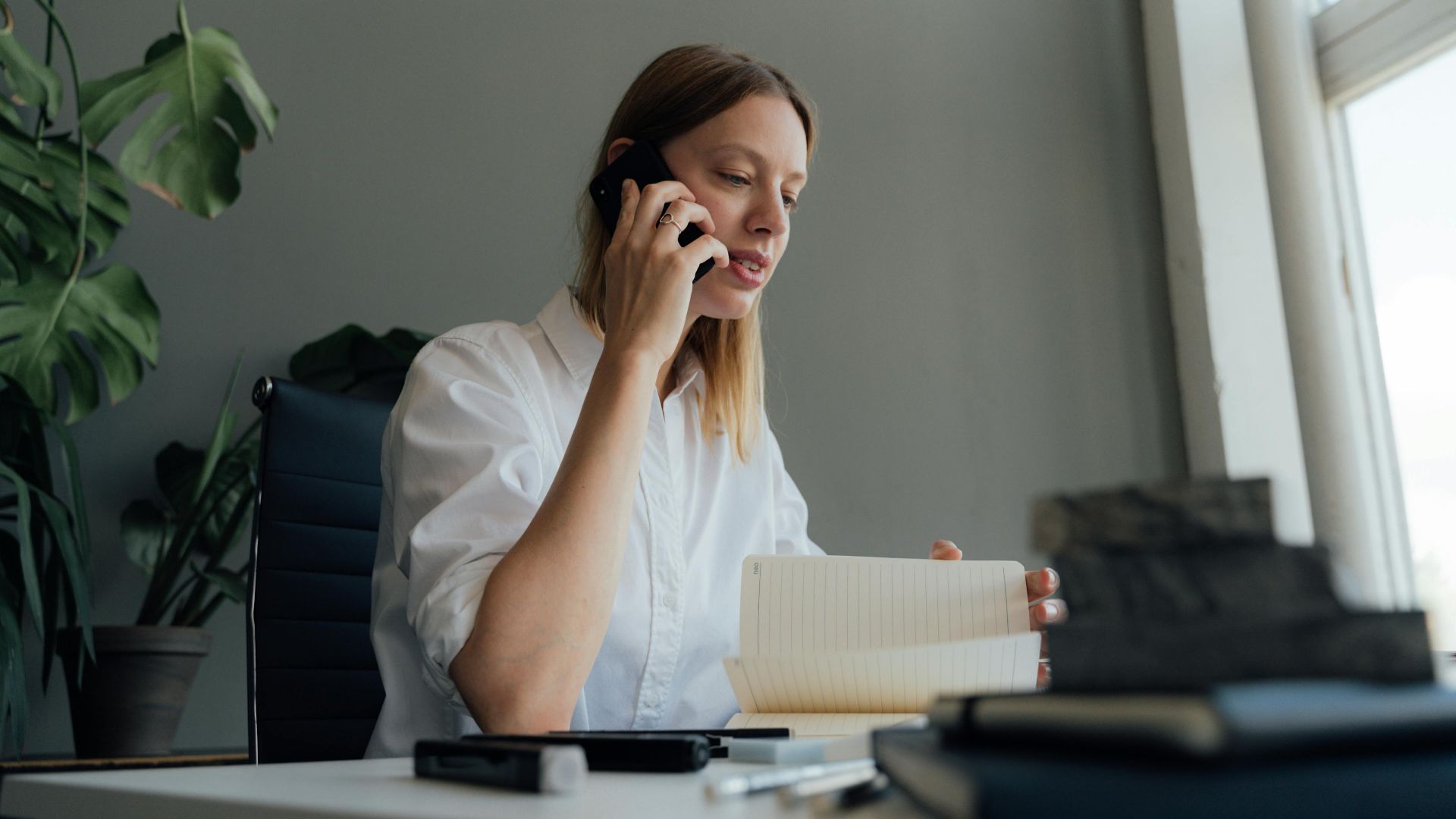 Woman on a phone call while reviewing documents at her desk indoors.