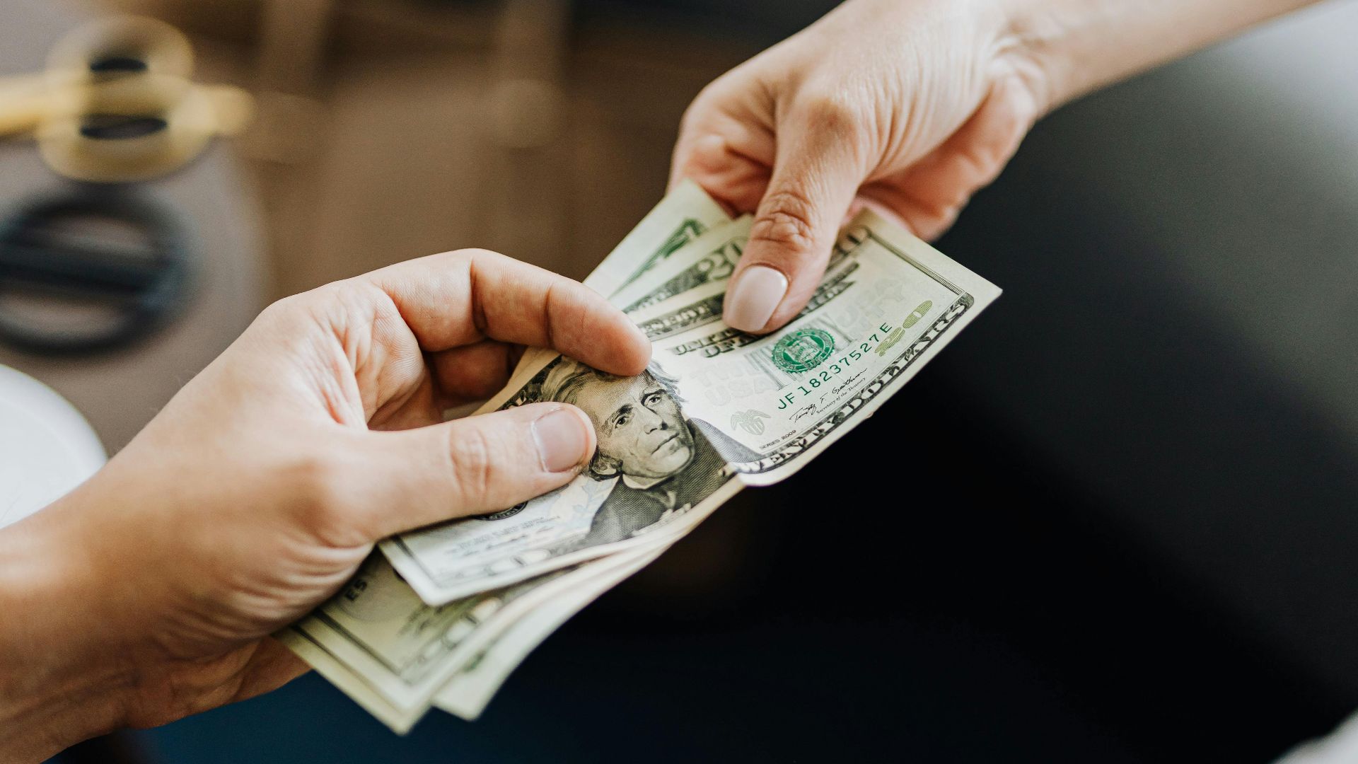 A close-up image of hands exchanging US dollar bills, symbolizing financial transaction or payment.
