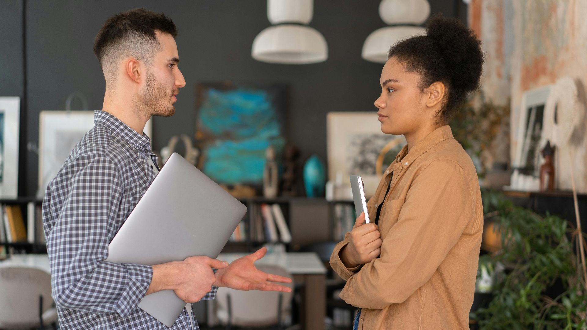 Two office workers engaged in a conversation, holding devices, in a modern office setting.