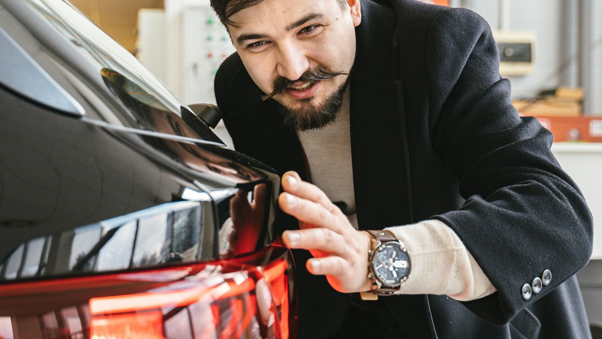 Man in business attire examining a car in an indoor setting, suggesting car maintenance or purchase.
