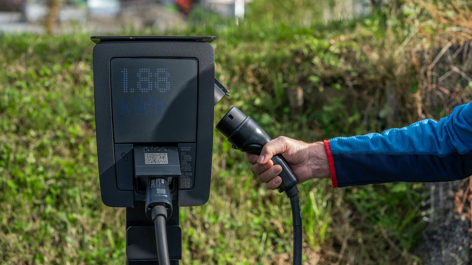 An outdoor electric car charging station with a hand holding a charging cable.