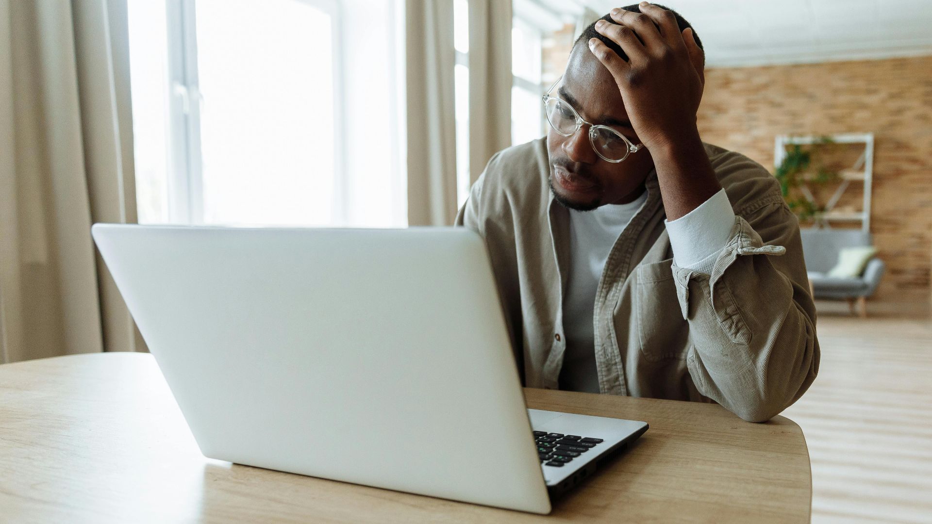 Man stressed while working on a laptop indoors, dealing with issues in remote work.