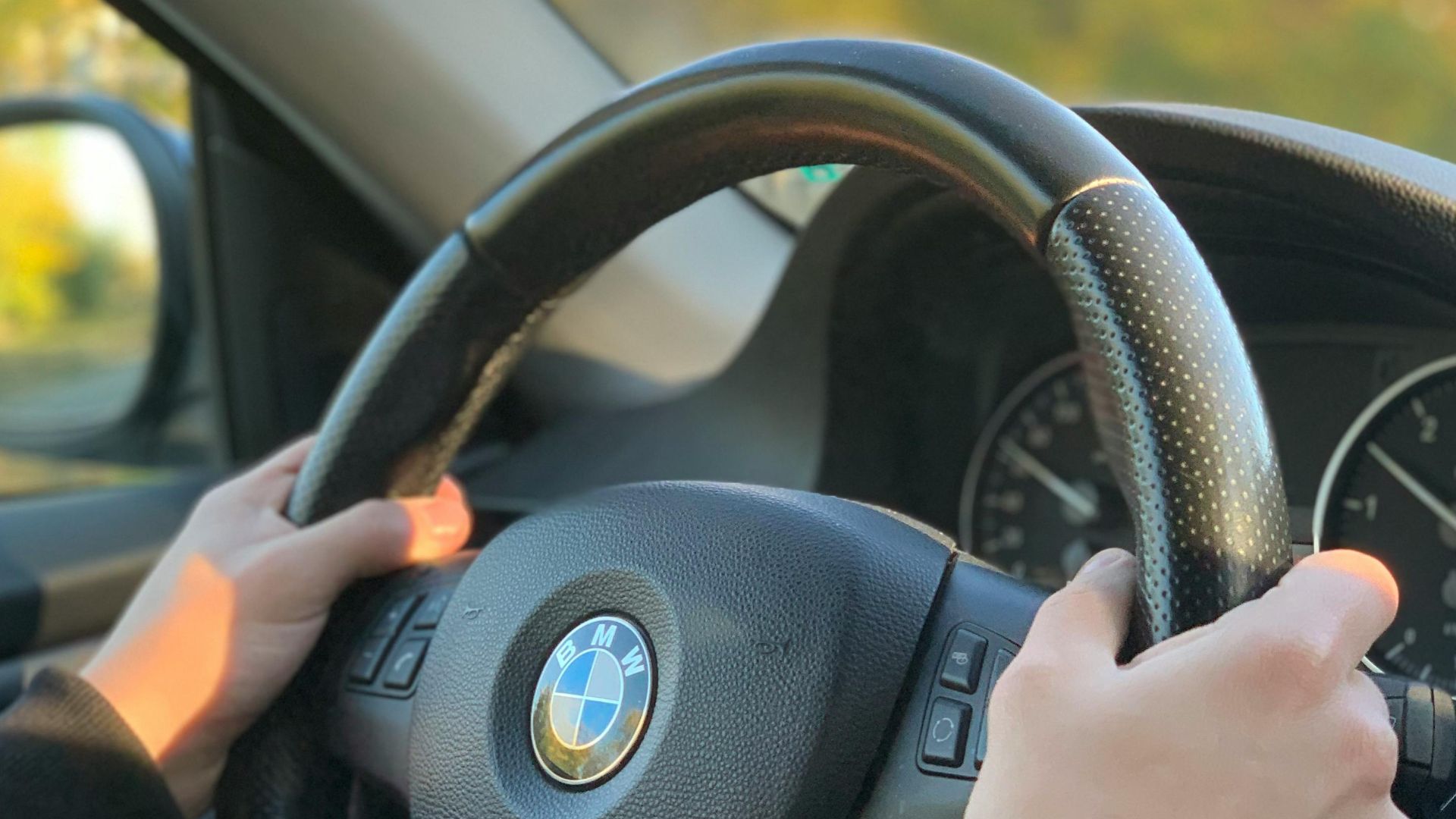 Hands gripping a BMW steering wheel inside a vehicle, captured in natural light.