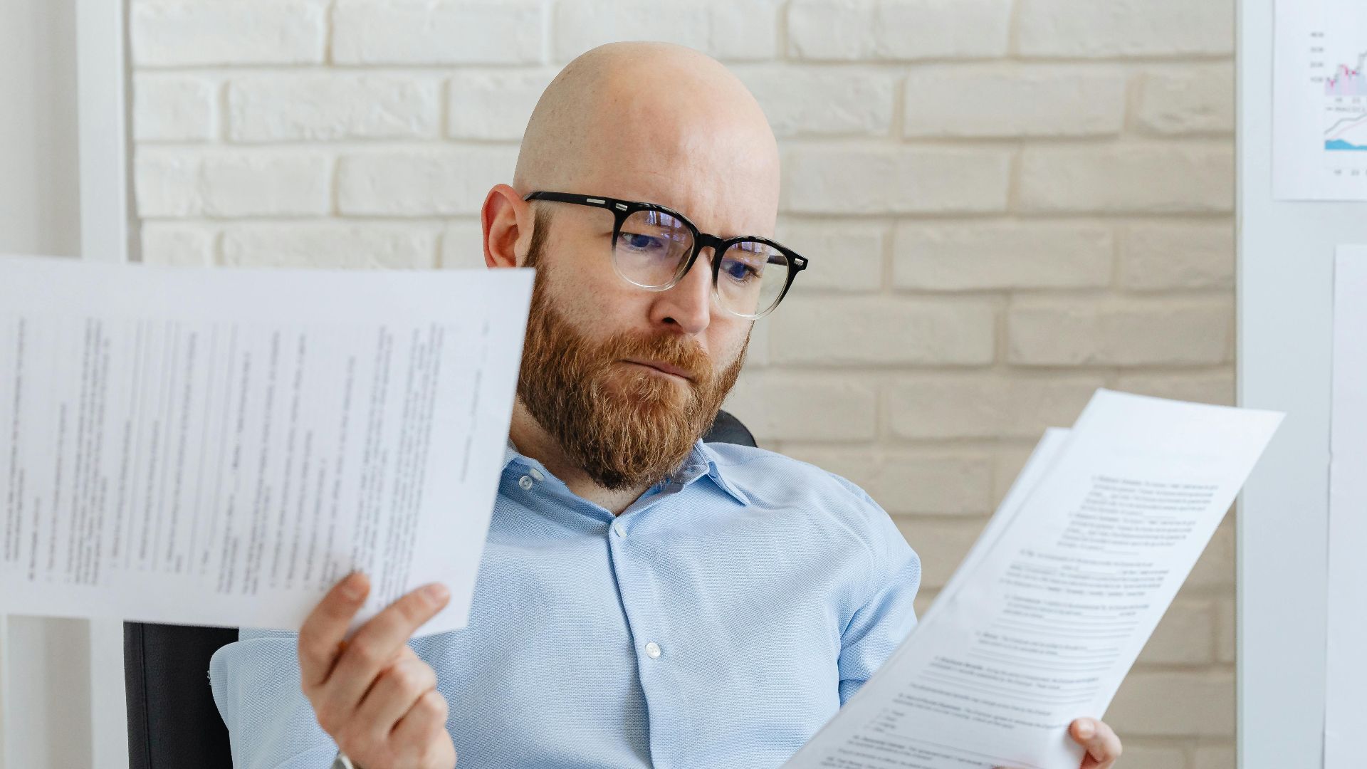 Bald bearded businessman reading financial documents in modern office setting.