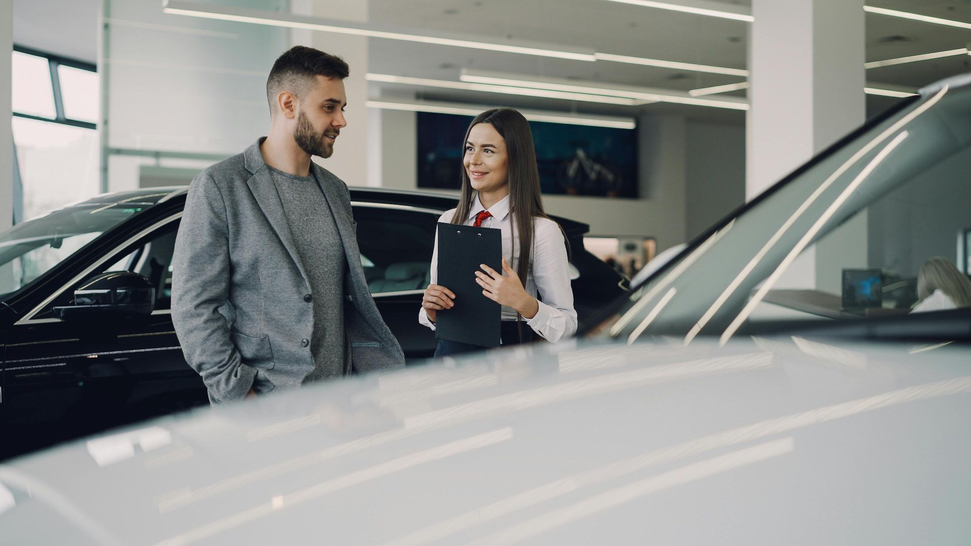 Man consults with salesperson in modern car dealership showroom.