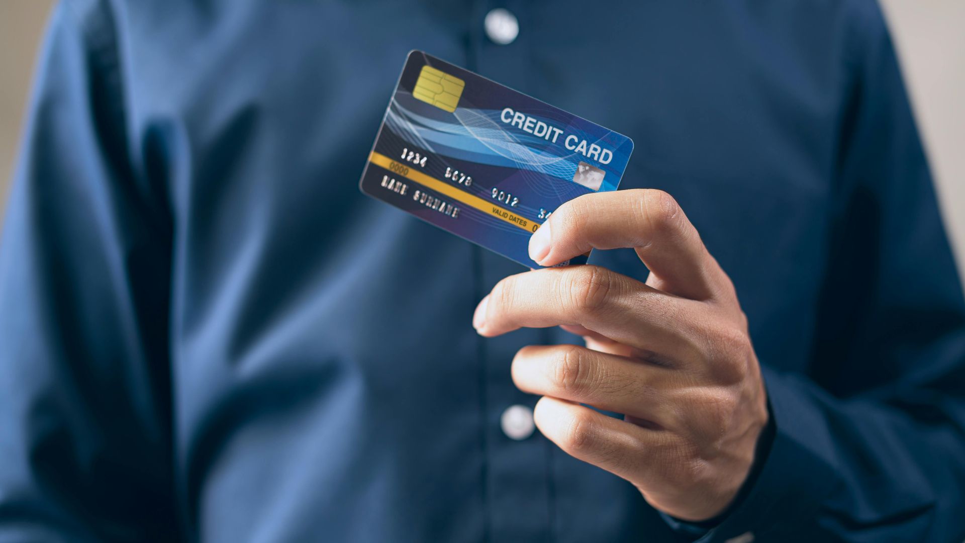 Close-up of a person holding a credit card in a hand, wearing a button-up shirt.