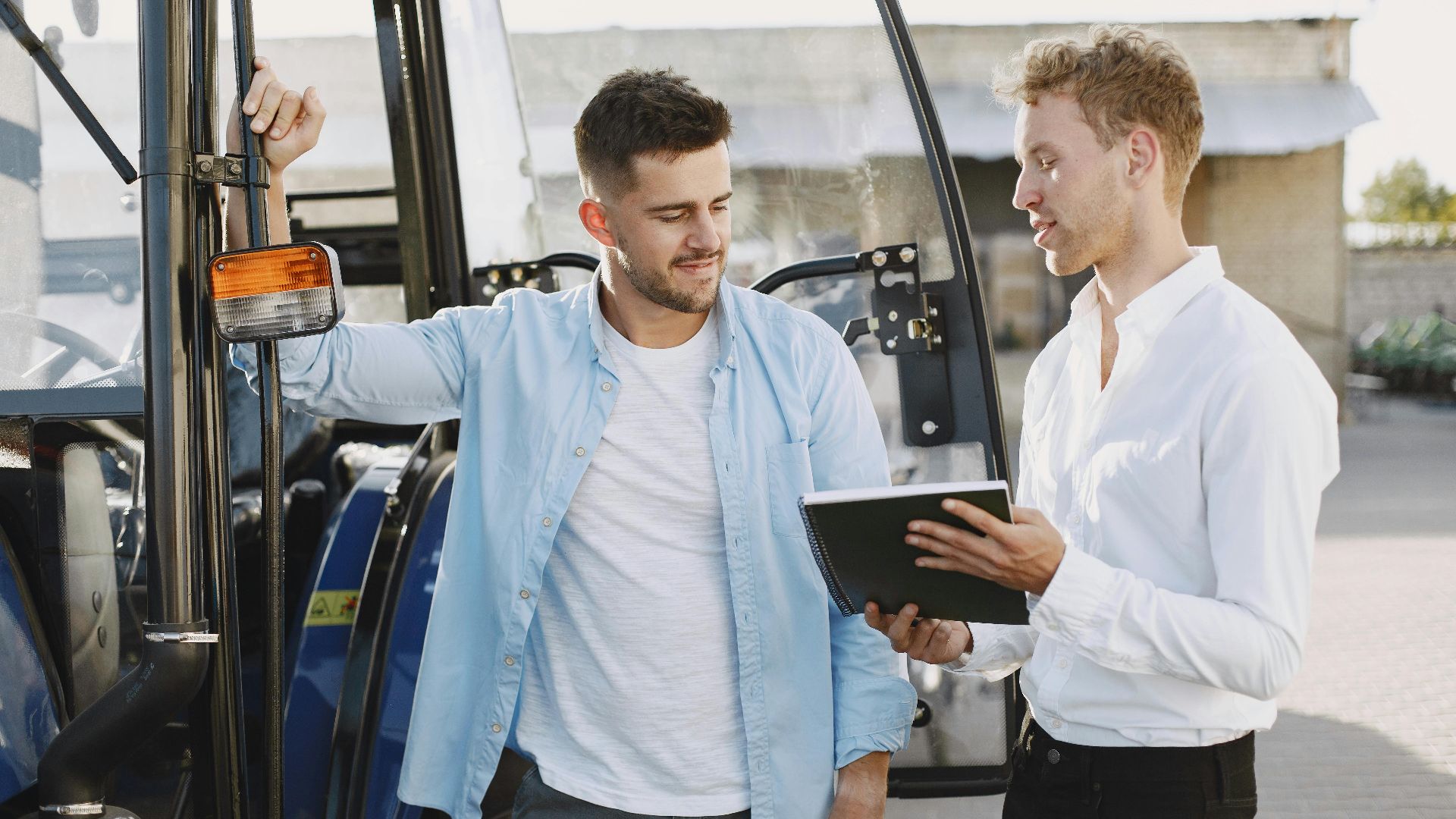 Two men discussing business plans beside a blue tractor outdoors.
