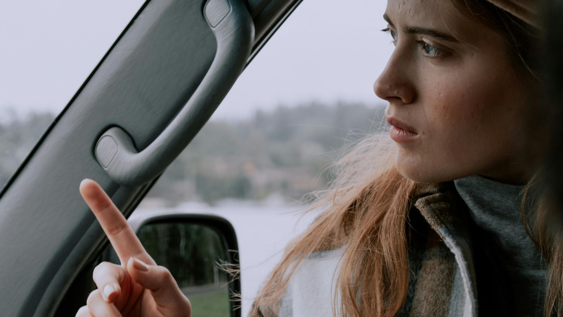 Woman in plaid jacket pointing while sitting inside a car, looking focused.