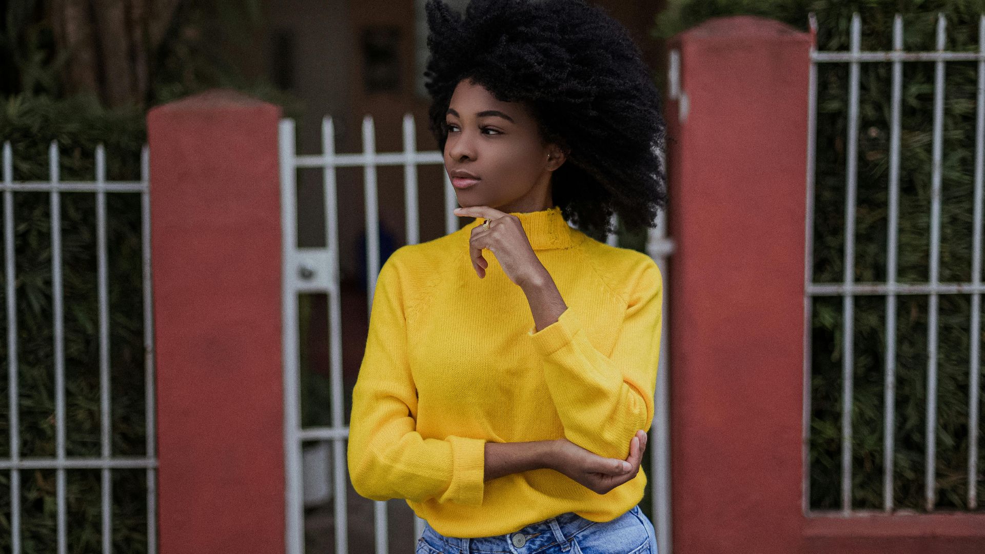 Young dreamy African American woman standing in wind touching chin and looking away